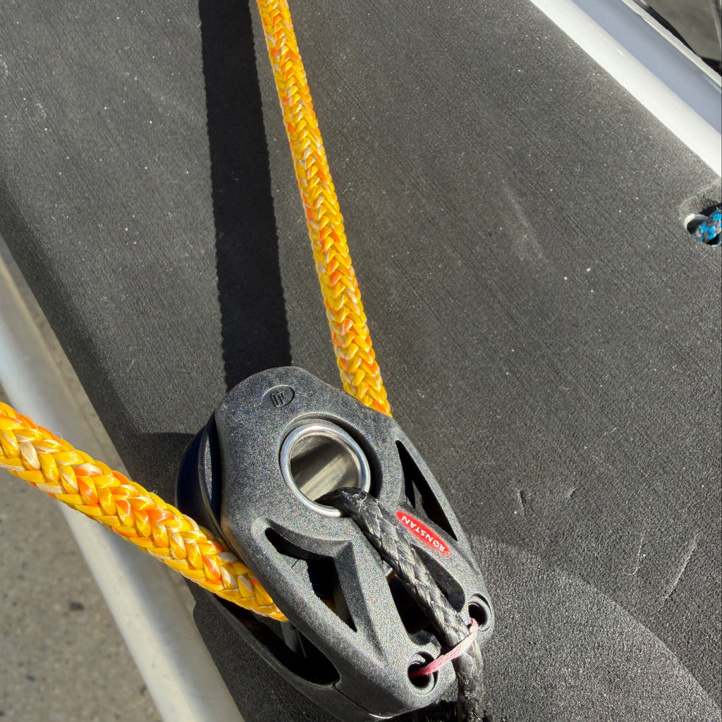 Close-up of a yellow rope attached to a black pulley system on a boat.